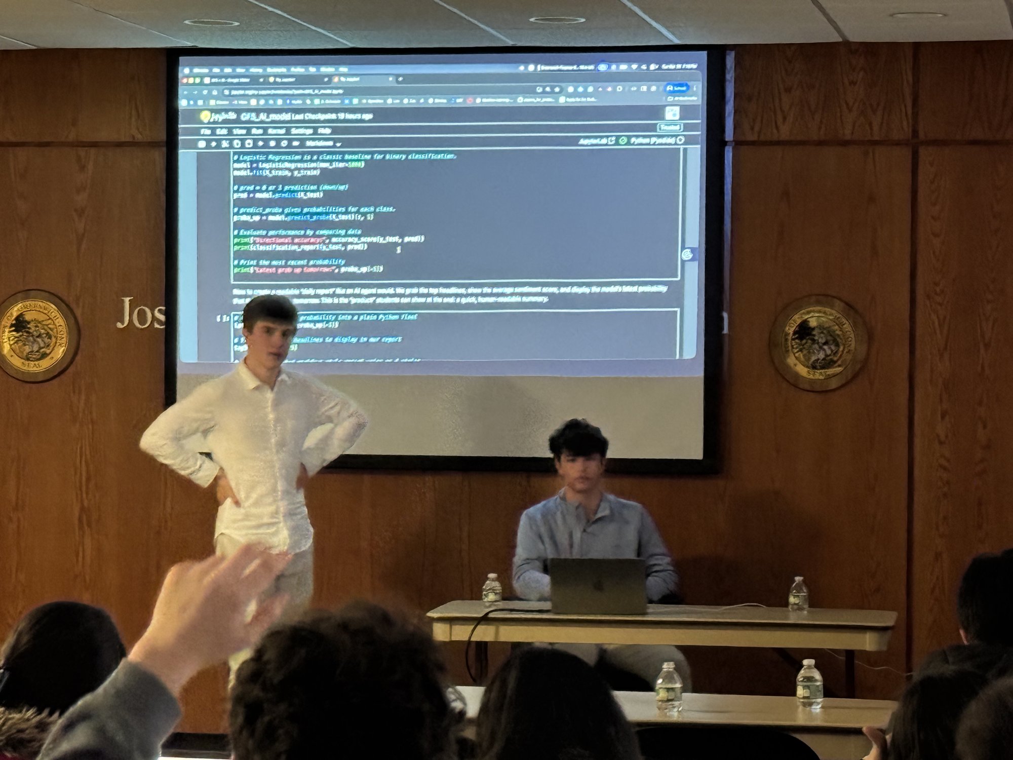 A student presenter standing in front of projected Python code explaining how the prediction model is assembled