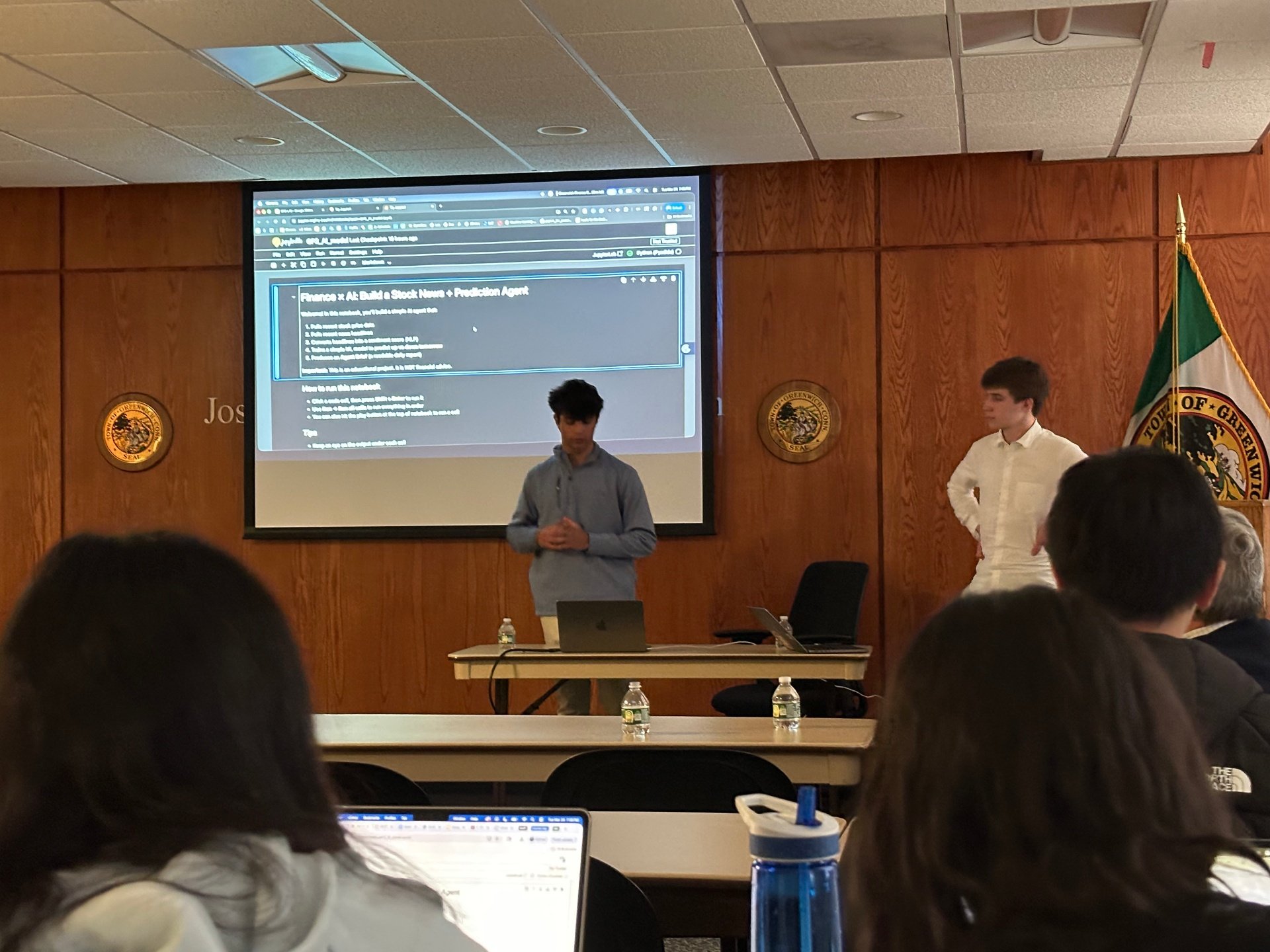 Two student presenters walking the room line by line through the stock-prediction notebook on the projector